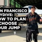 Tandem skydiving student wearing San Francisco Giants jacket in front of small airplane, preparing for a skydive near San Francisco